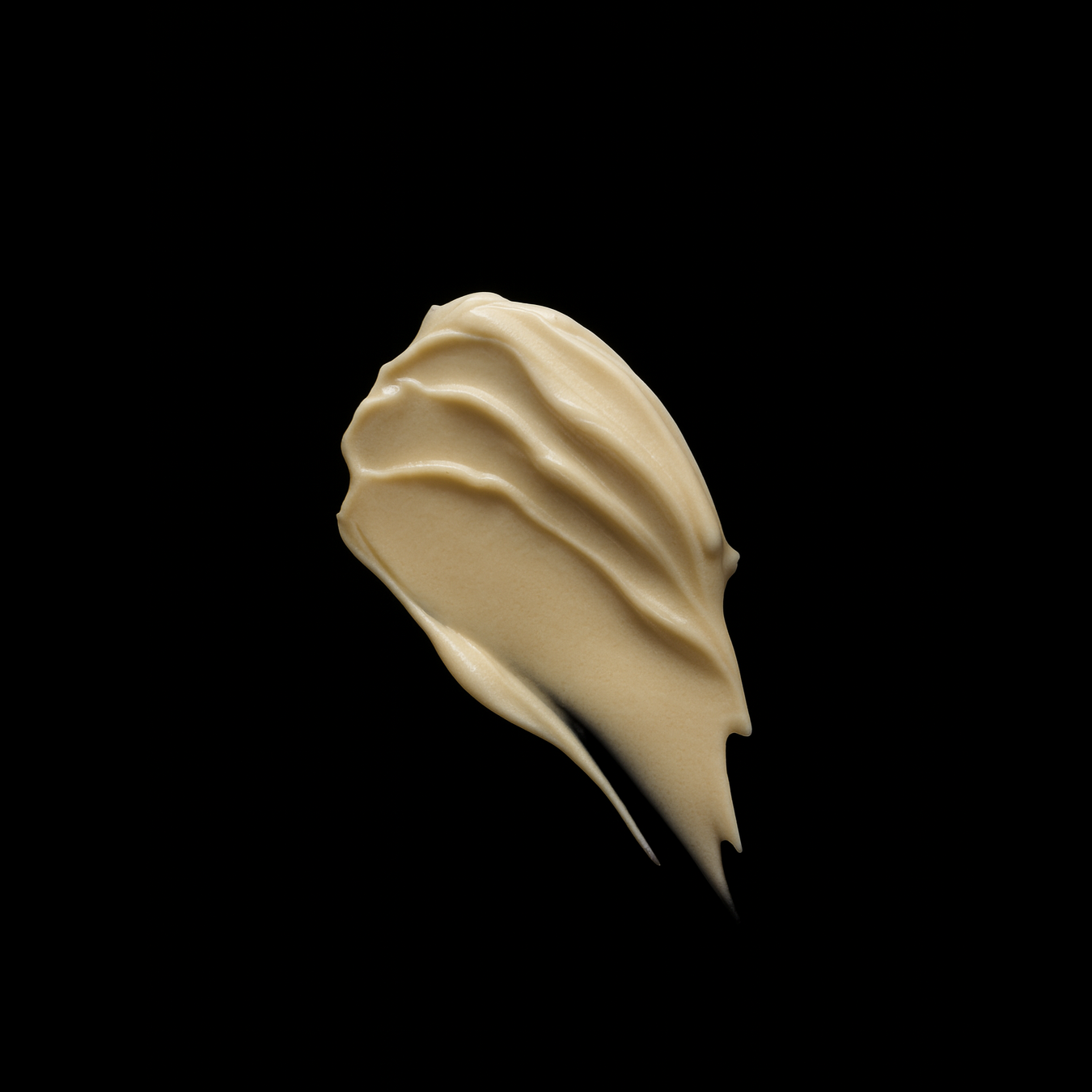 Eine Nahaufnahme eines cremigen, beigefarbenen Produktstreichs, der die reichhaltige Textur der "BYOCREAM" auf einem kontrastierenden schwarzen Hintergrund zeigt.