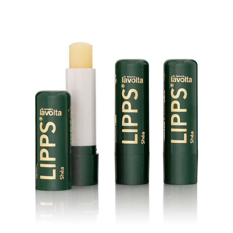 Drei Dr. Armah's Lavolta LIPPS Shéa Lippenpflegestifte, einer davon geöffnet (Three Dr. Armah's Lavolta LIPPS Shéa lip care sticks, one of them open).