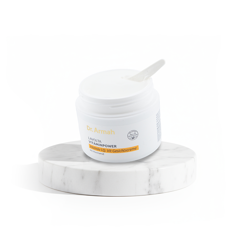 Ein geöffneter Tiegel der Dr. Armah LAVOLTA VITAMINPOWER Gesichtscreme mit einem Spatel, präsentiert auf einem runden Marmorpodest vor weißem Hintergrund.