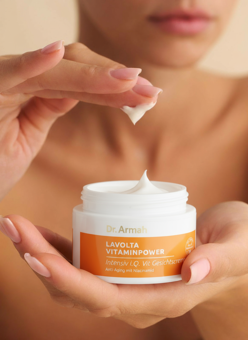 In einer Nahaufnahme sind die Hände einer Frau zu sehen, die einen offenen Tiegel "Dr. Armah Vitaminpower" Gesichtscreme halten. Mit einem Finger entnimmt sie eine kleine Menge der weißen, reichhaltigen Creme aus dem Tiegel.